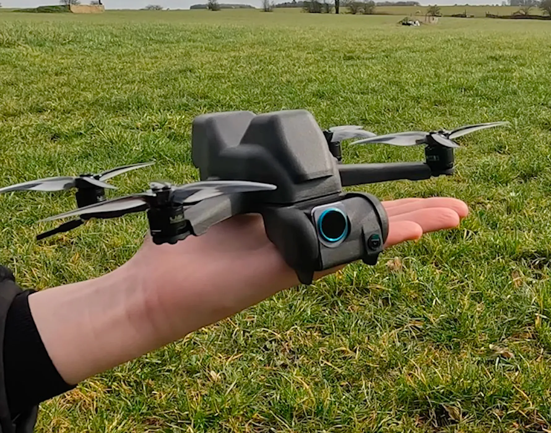 手のひらにのせられた小型の黒いドローンが草原の前景にある。