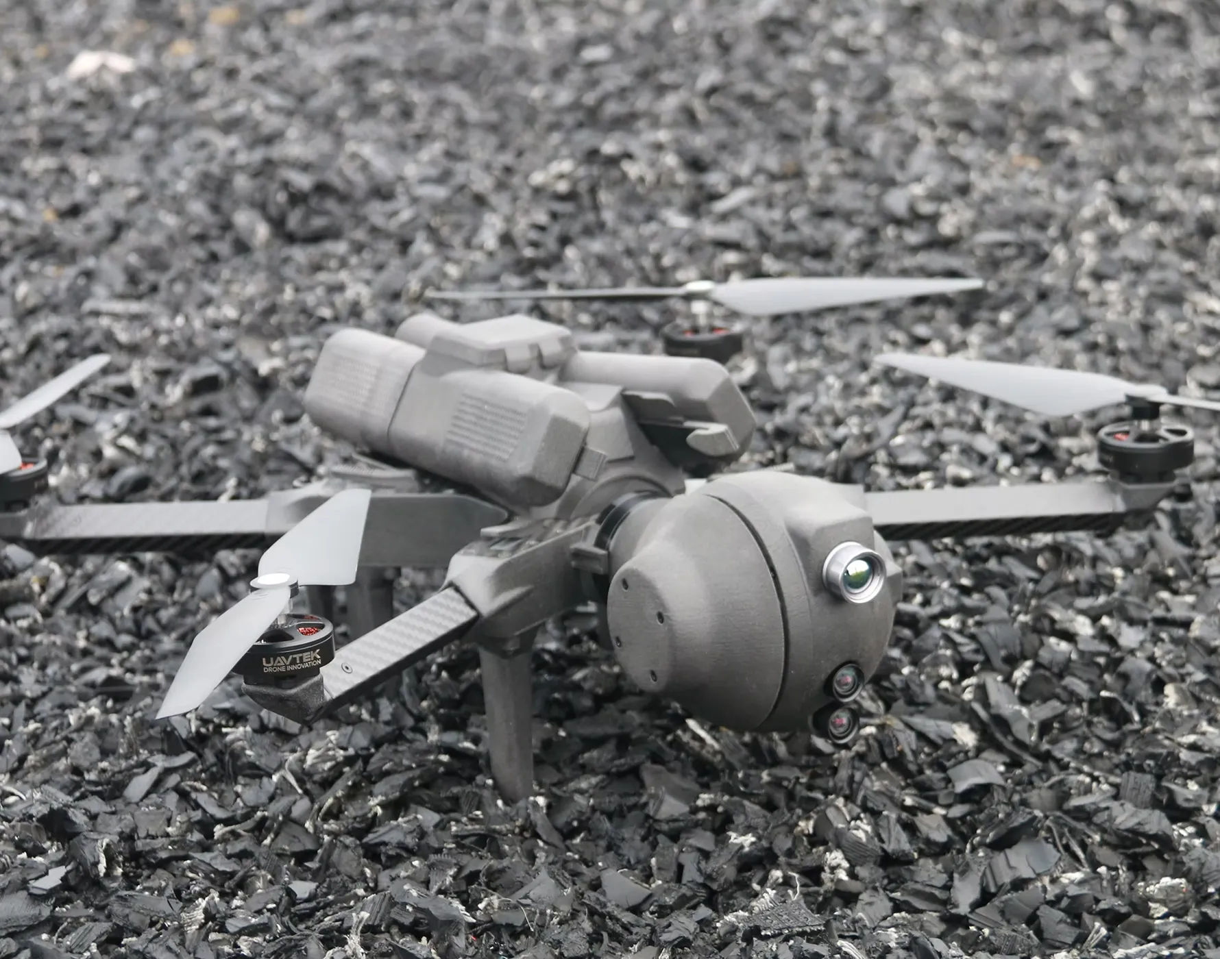 地面に置かれたカーボンファイバー製アームを持つ黒い多ロータードローンで、前方に複数のカメラやセンサーが搭載されている。