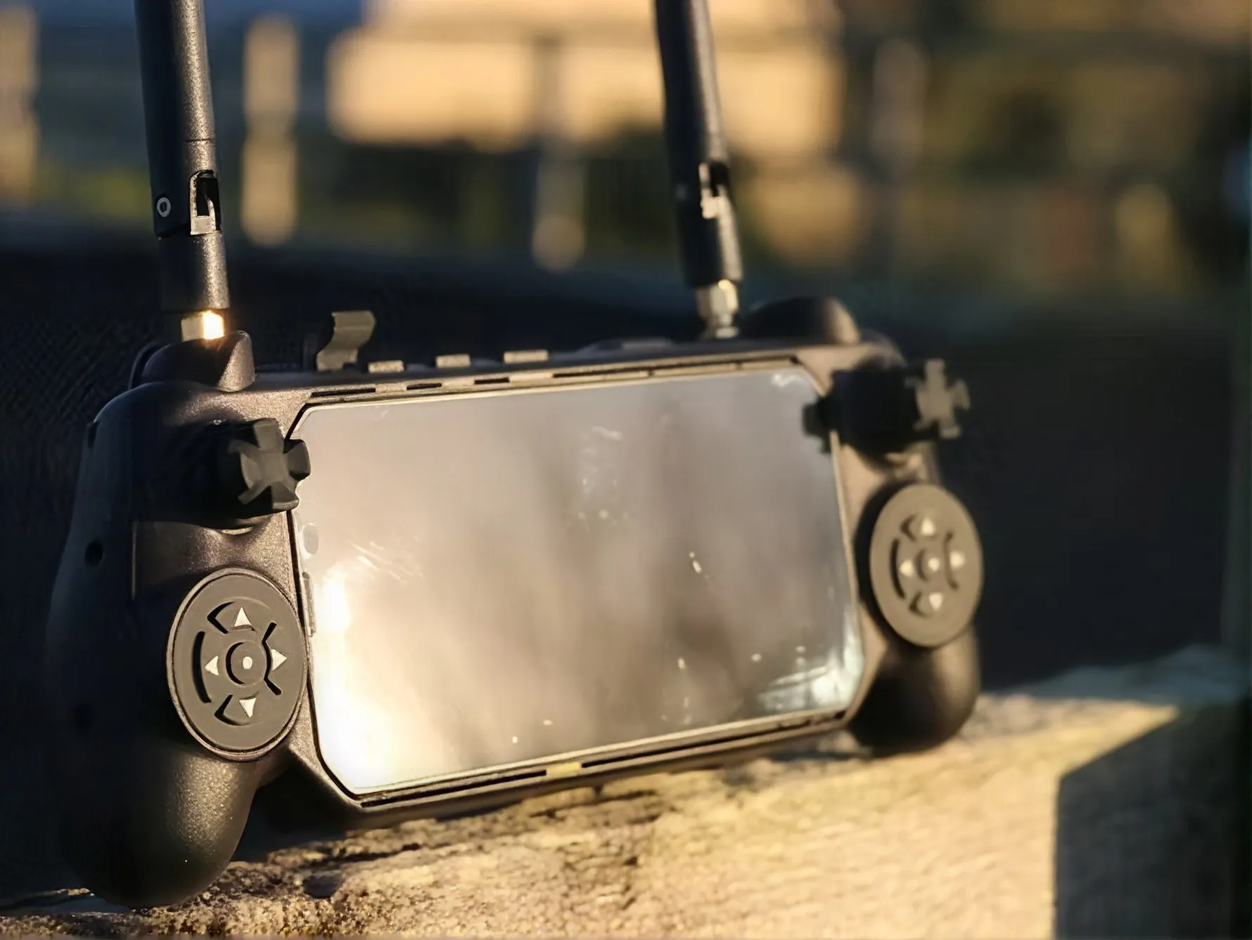 携帯電話を取り付けた黒いゲームコントローラー、背景にぼやけた屋外の景色。