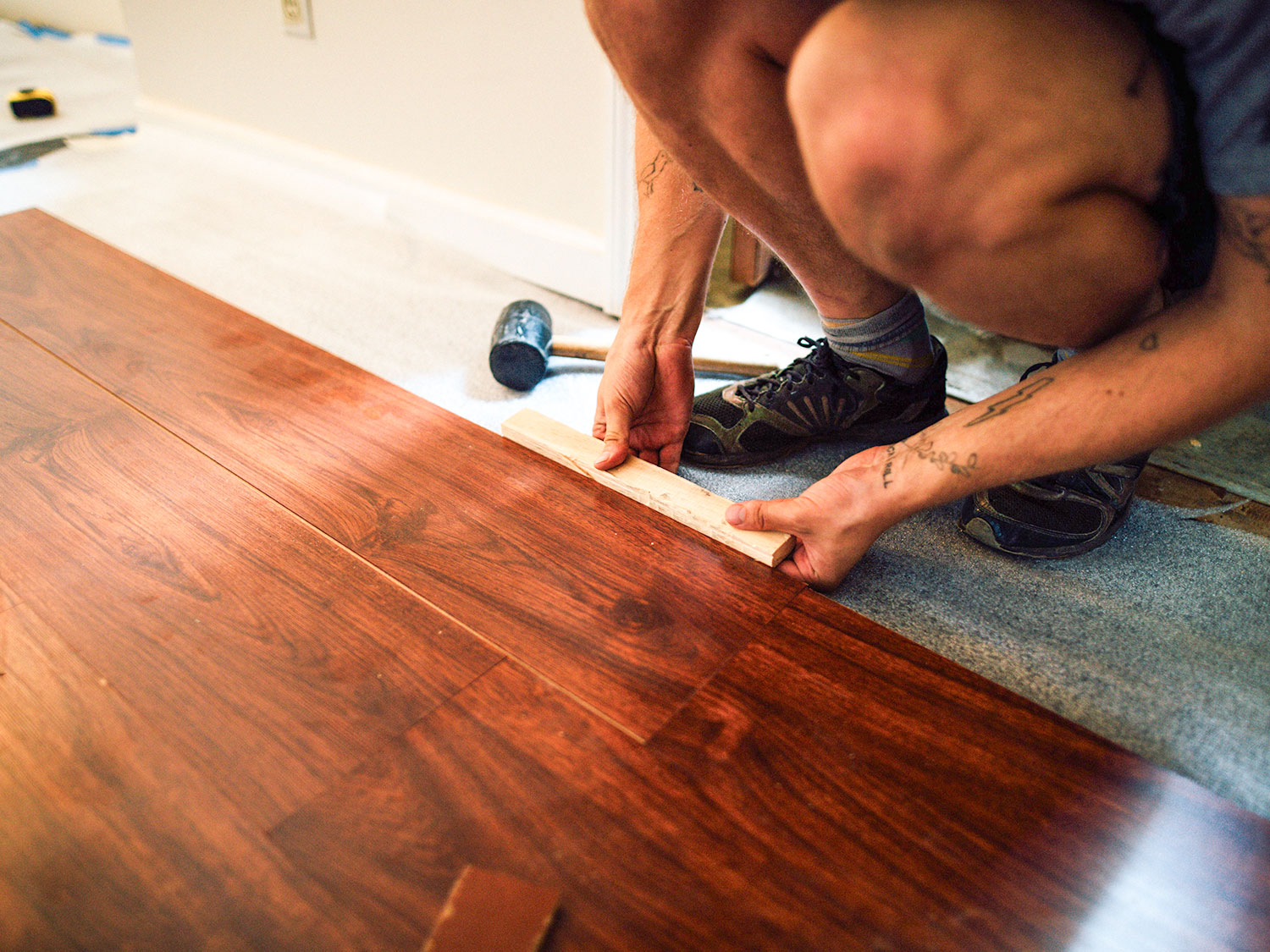 Handwerker verlegt dunkle Holzdielen mit Schlagholz und Gummihammer.