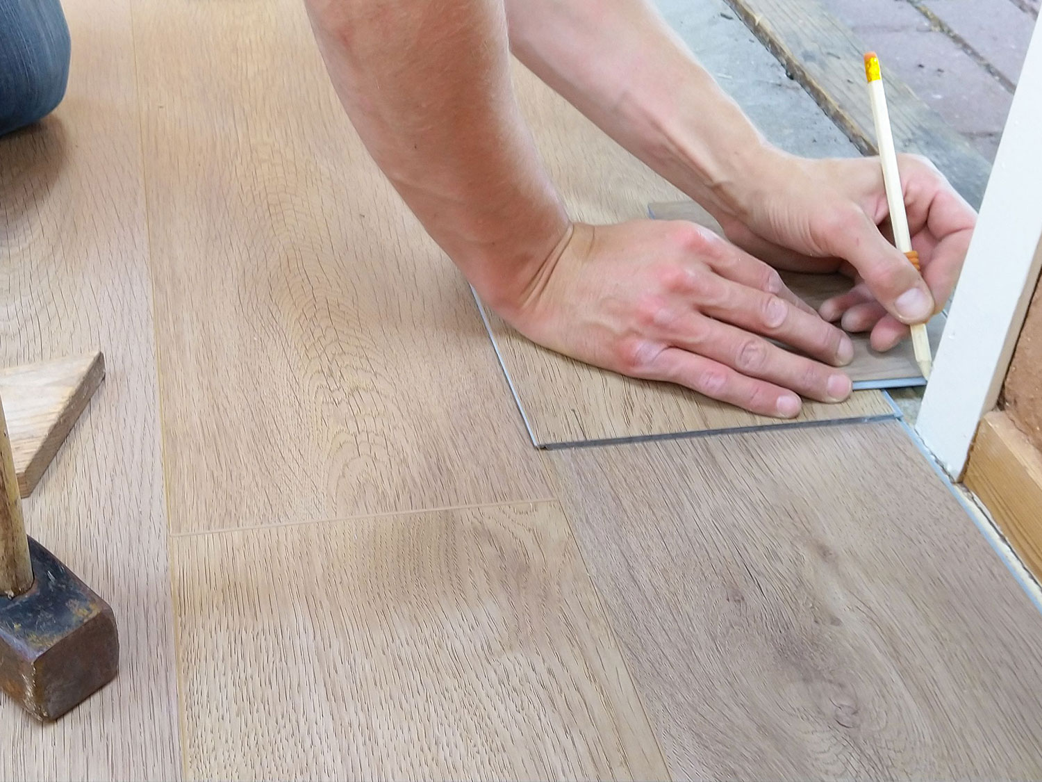 Handwerker zeichnet mit Bleistift eine helle Eichendiele zum Zuschneiden an.