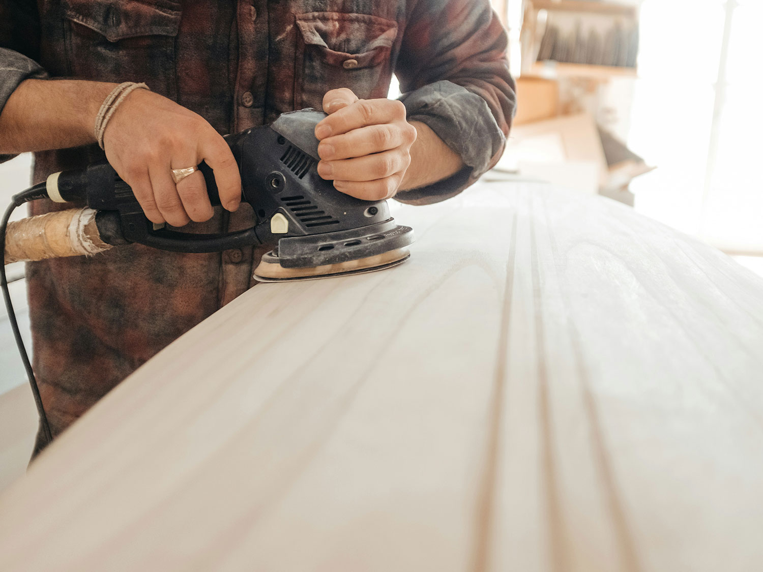 Handwerker schleift eine helle Holzoberfläche mit einem Exzenterschleifer.