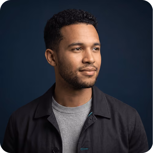 Studio headshot of a man in a dark jacket looking to the side against a navy backdrop