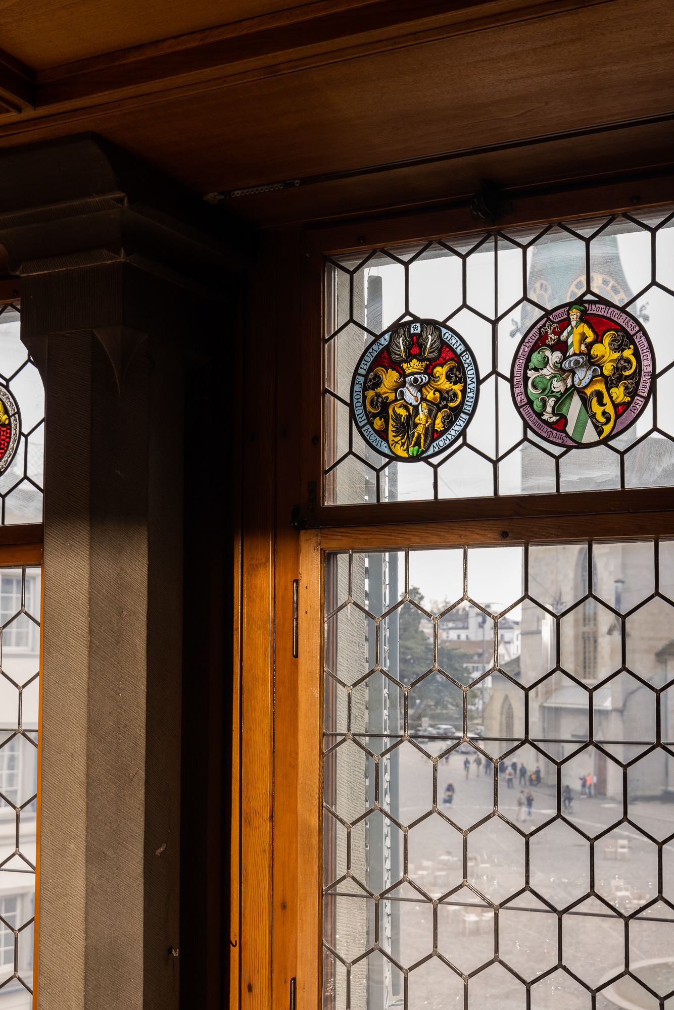 Leaded window with two round heraldic panels and a view of the Münsterhof