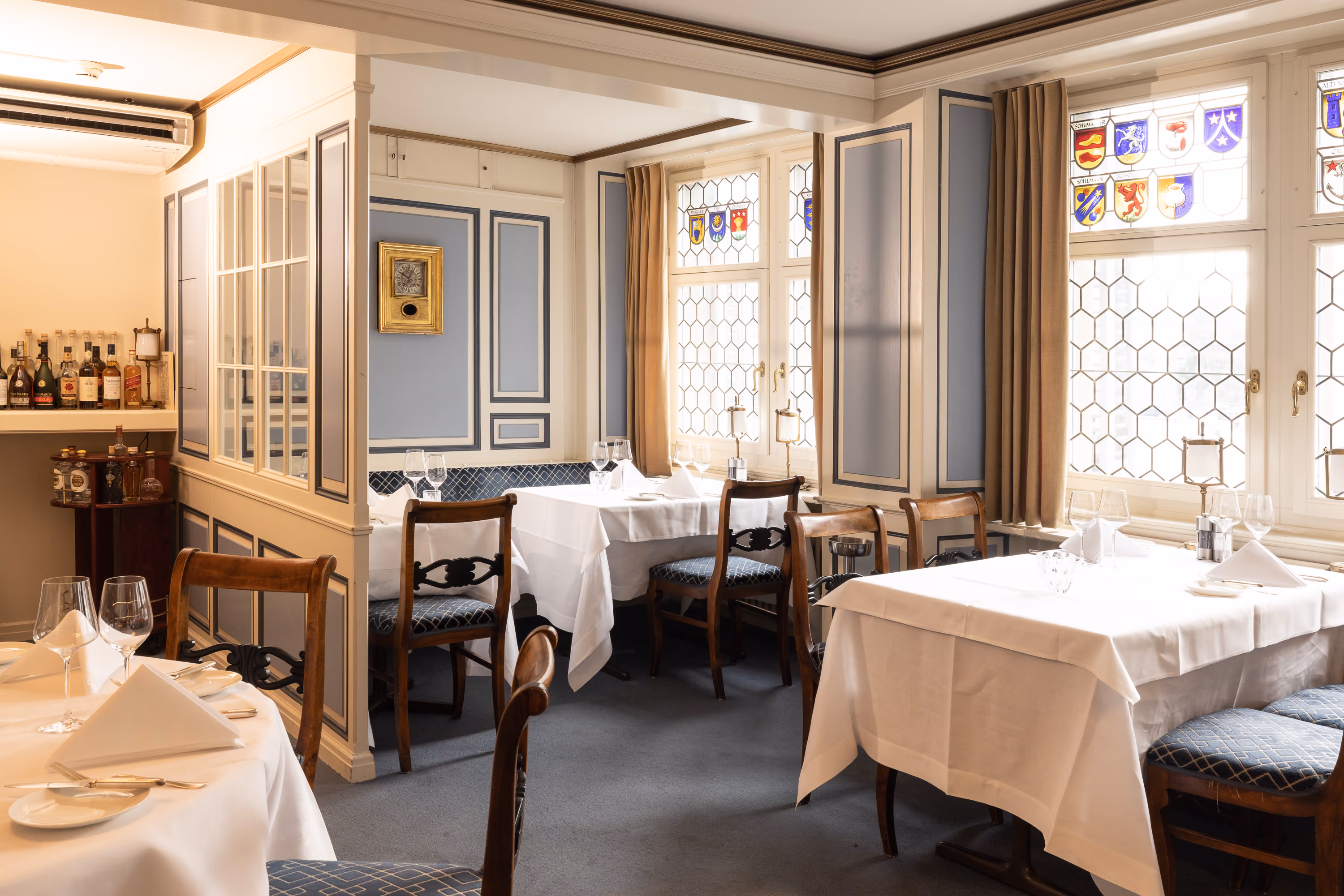 Restaurant im Zunfthaus zur Waag mit gedeckten Tischen, Wappenscheiben in den Fenstern und kleiner Bar