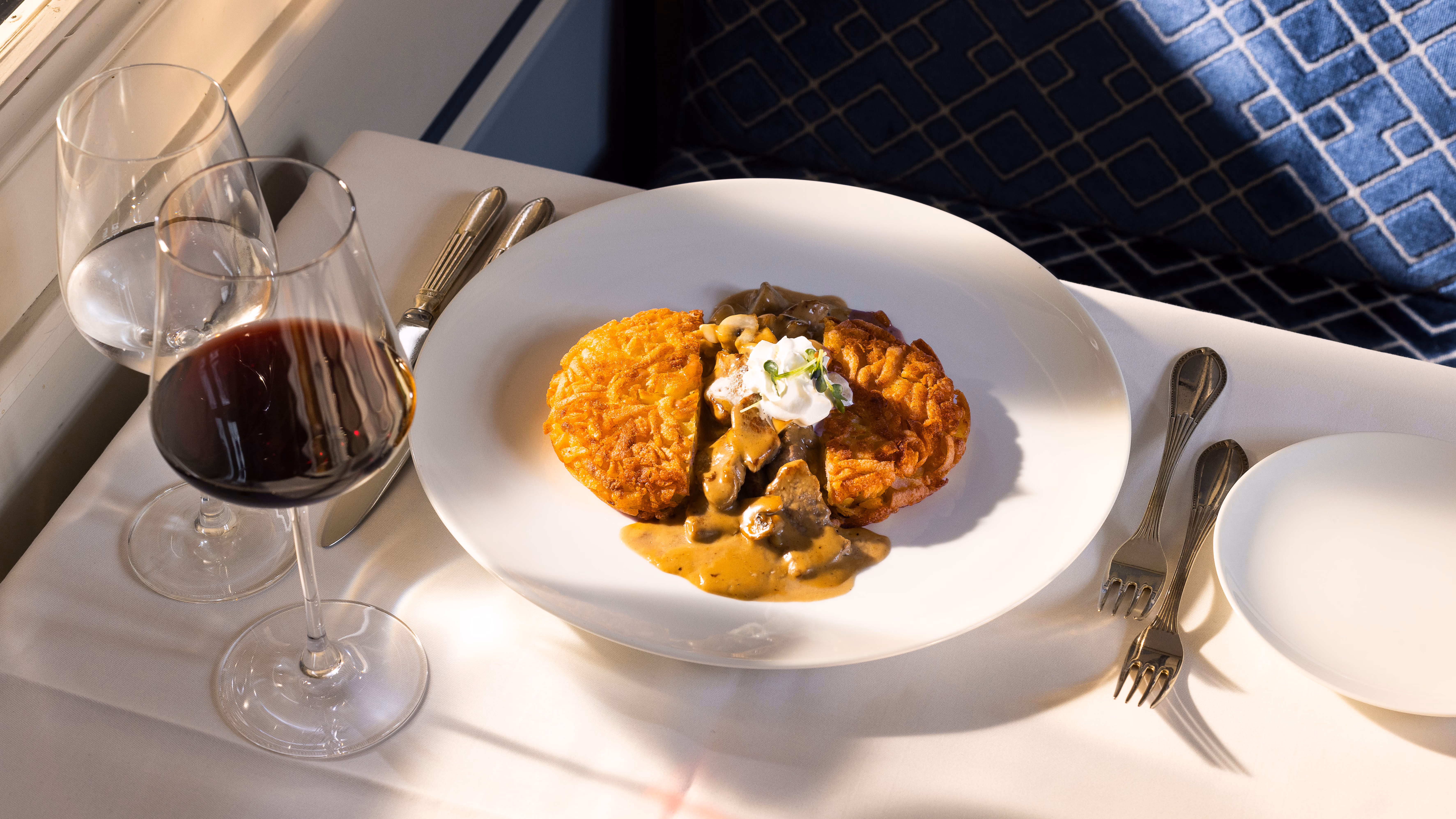 Zürcher Geschnetzeltes mit Rösti und Rahmsauce, daneben ein Glas Rotwein am Fensterplatz