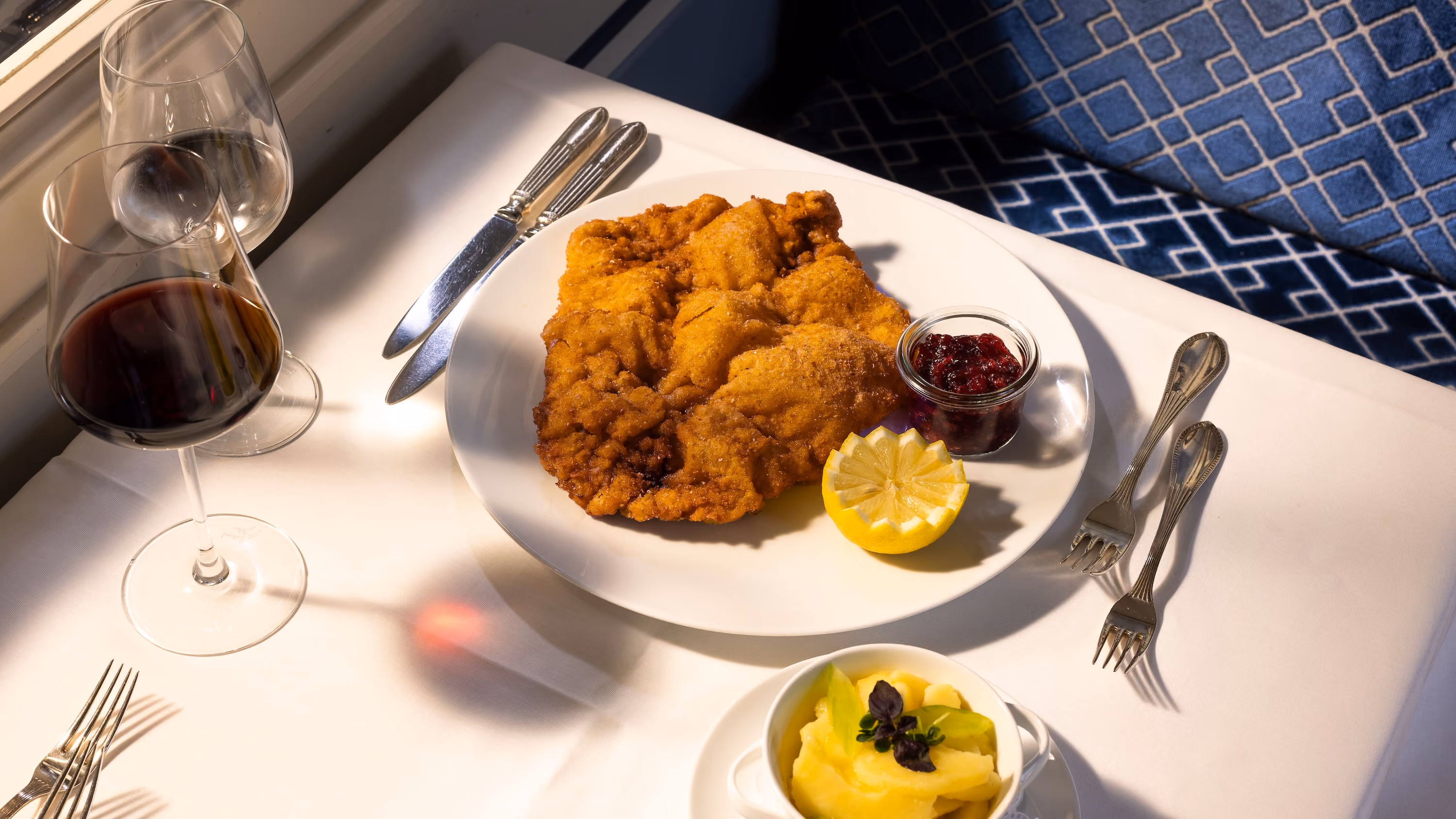 Wiener Schnitzel mit Zitrone und Preiselbeeren, dazu Kartoffelsalat und ein Glas Rotwein