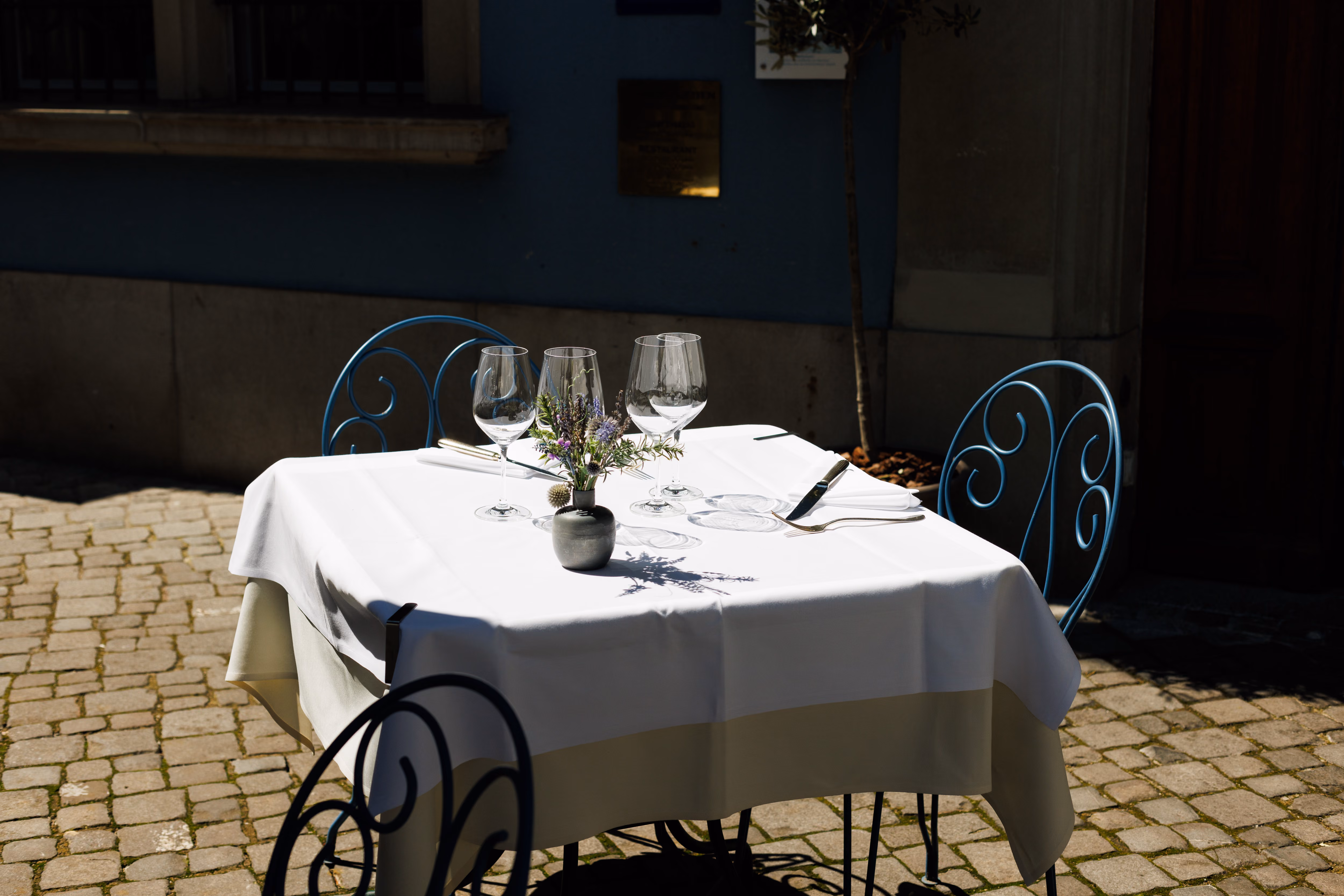 Weiss gedeckter Terrassentisch mit Weingläsern und Blumen auf dem Kopfsteinpflaster vor dem Zunfthaus zur Waag