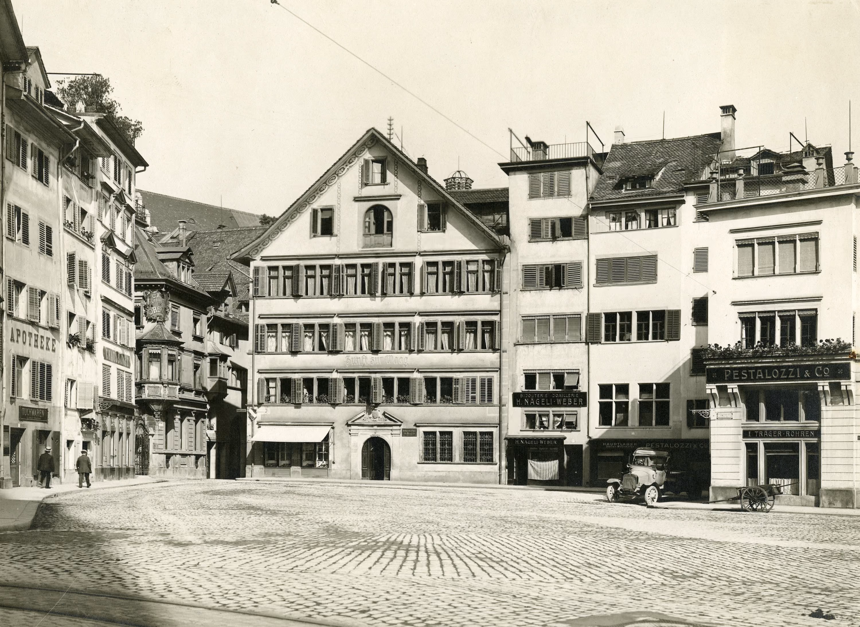 Historische Schwarzweissaufnahme des Zunfthauses zur Waag am gepflasterten Münsterhof mit Oldtimer