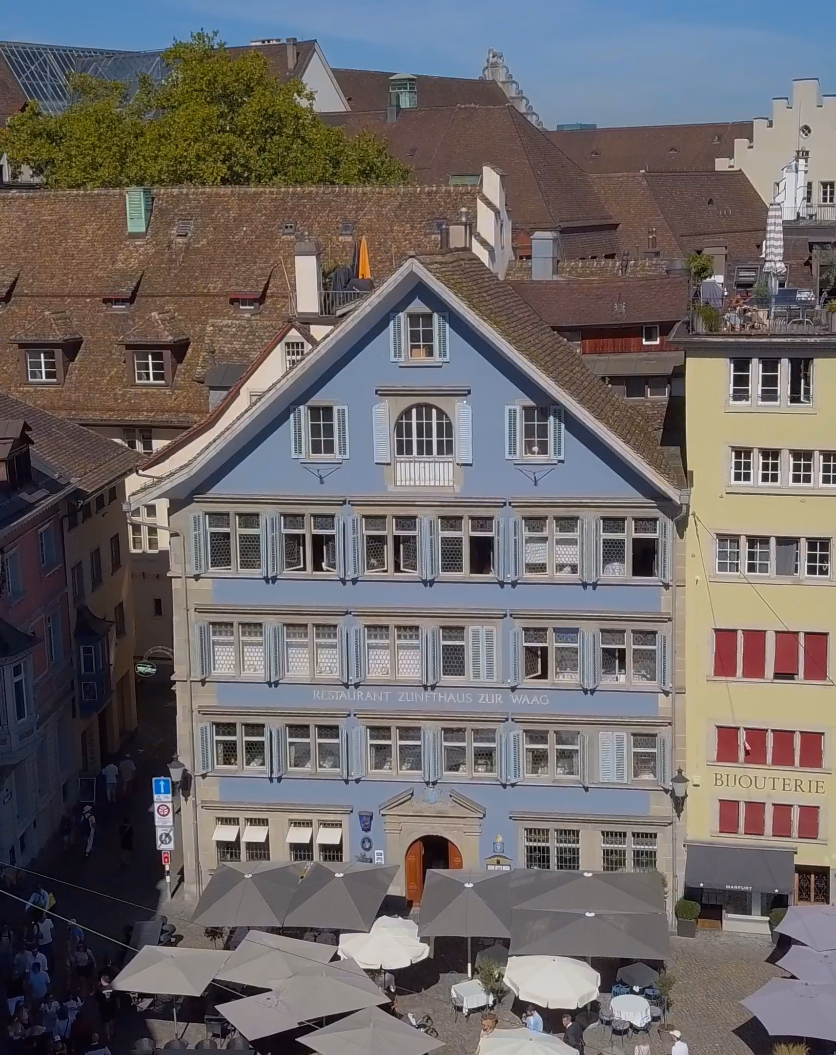 Hellblaue Fassade des Zunfthauses zur Waag am Münsterhof in Zürich mit Sonnenschirmen der Terrasse