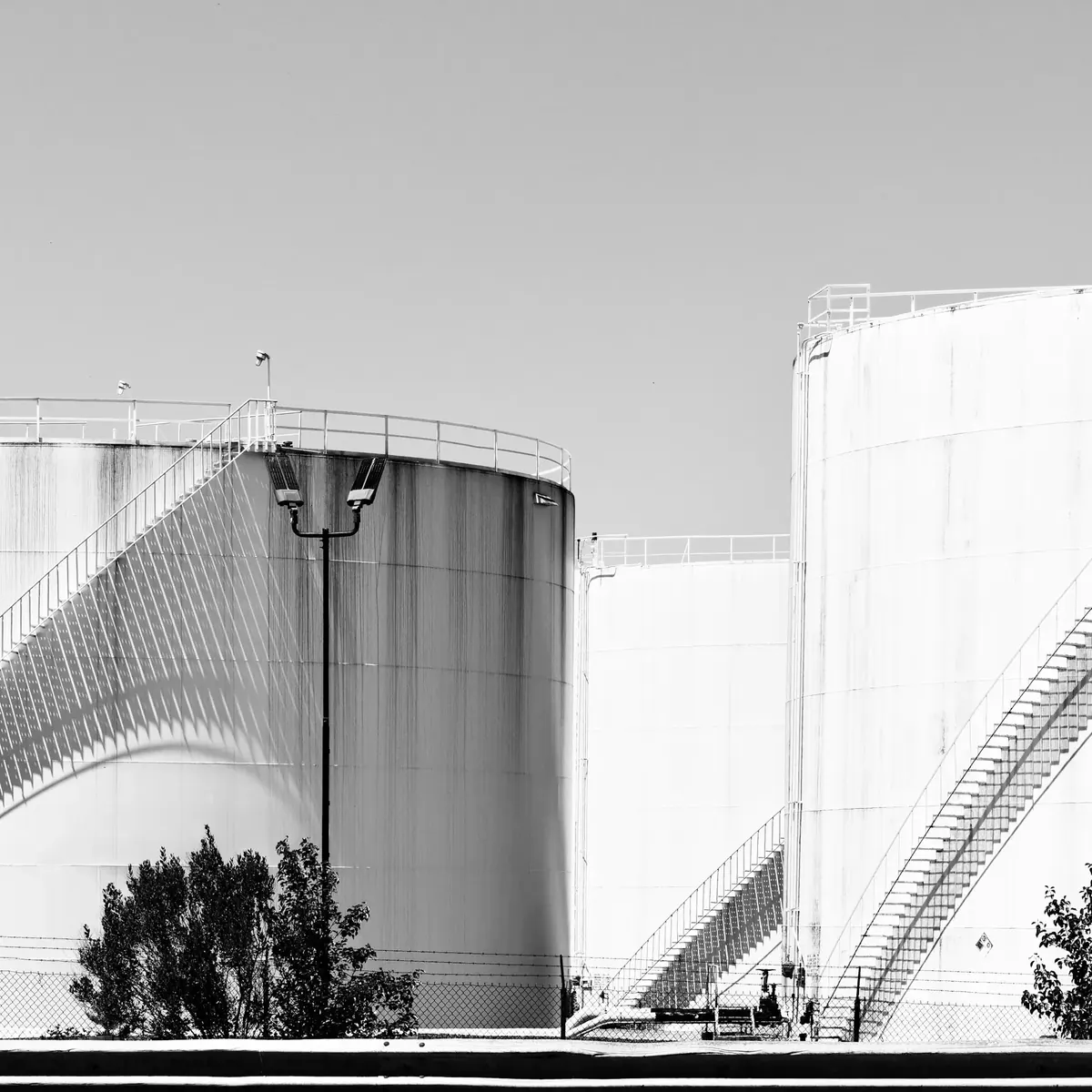 Large white industrial storage tanks with external stairways, in black and white