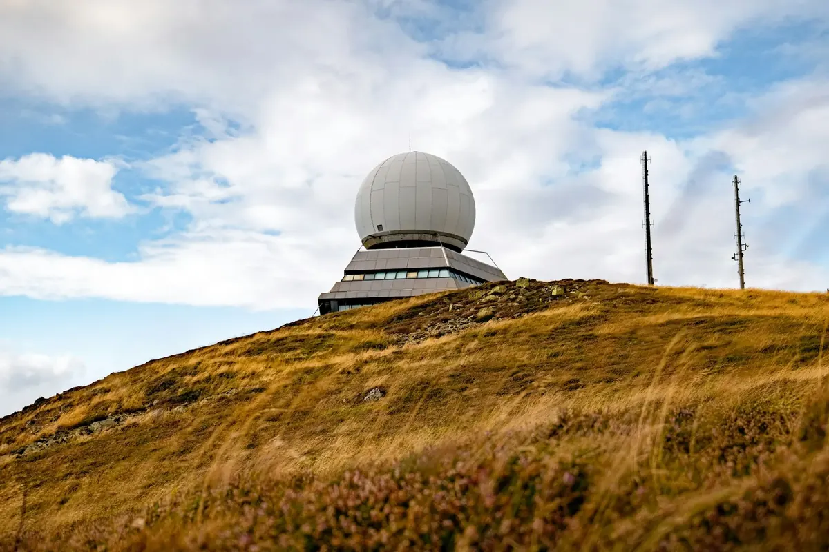 A radar dome on a grassy hilltop under a cloudy sky