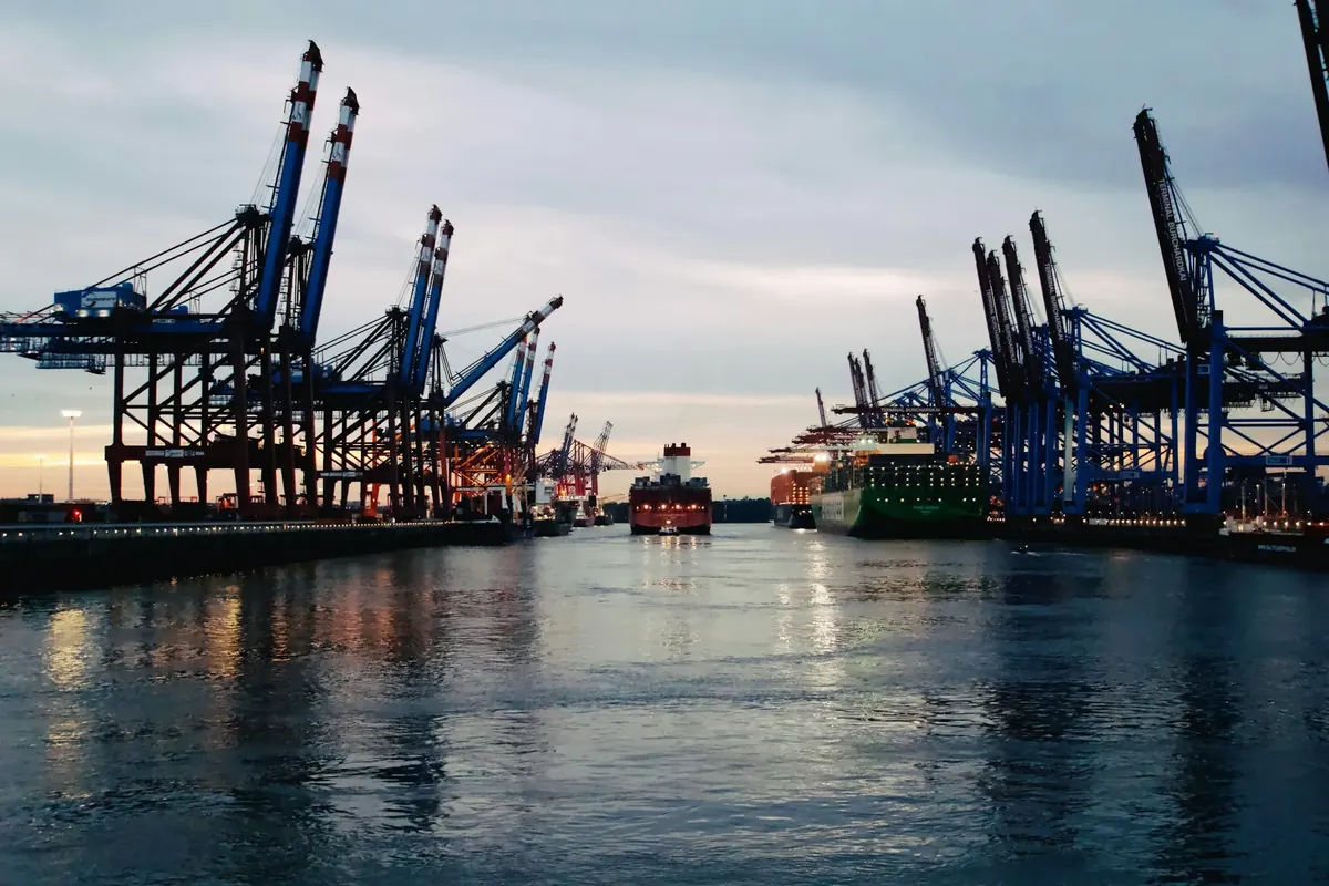Container cranes and cargo ships along a channel in the Port of Hamburg at dusk