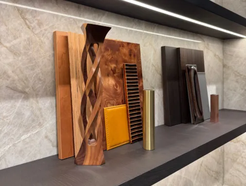 Vitrine avec plusieurs échantillons de bois décoratifs et une pièce métallique cylindrique sur une étagère en métal dans un environnement moderne.