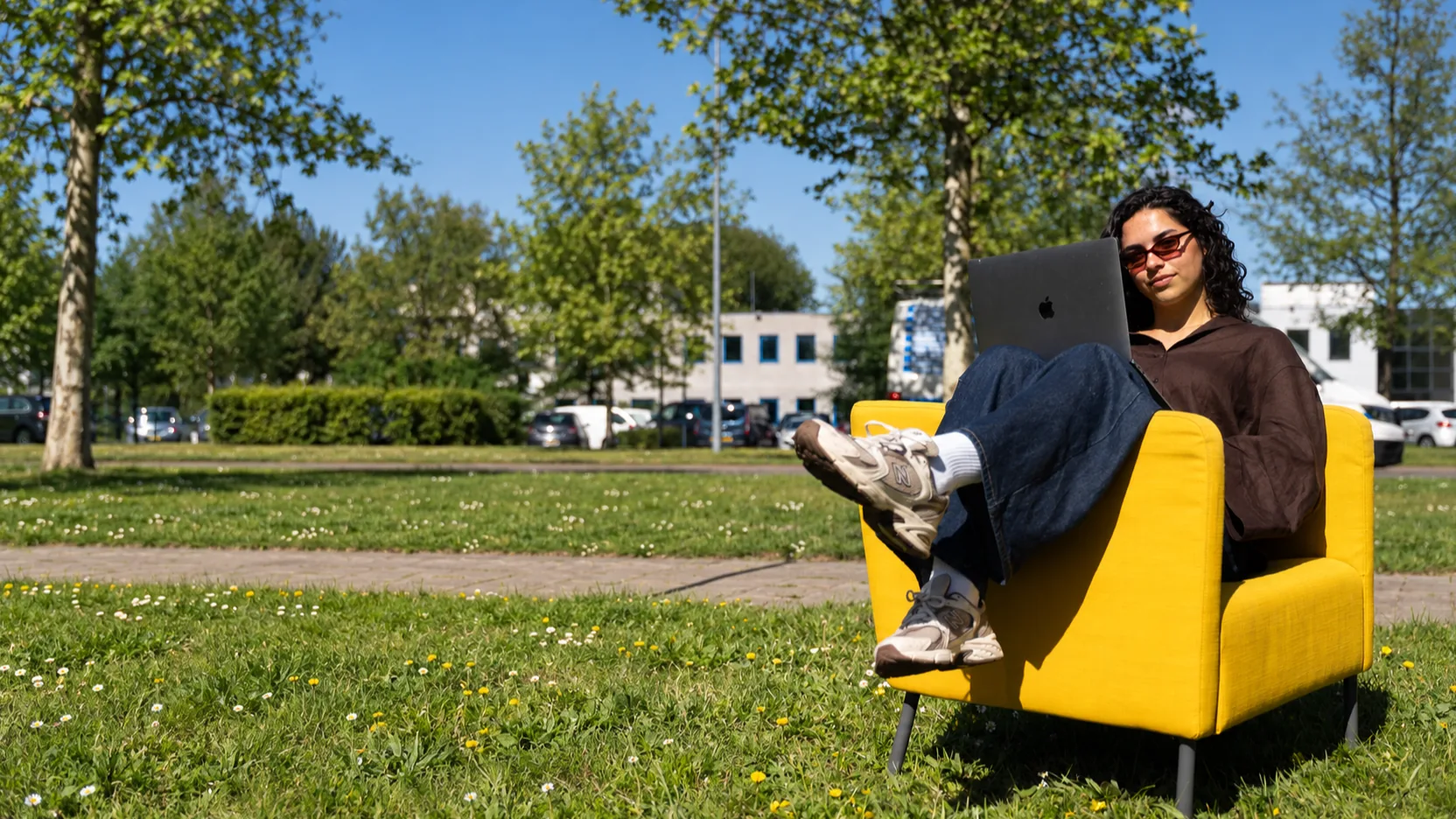Izara from Pro Contact with a laptop in a yellow chair on the grass outside the office