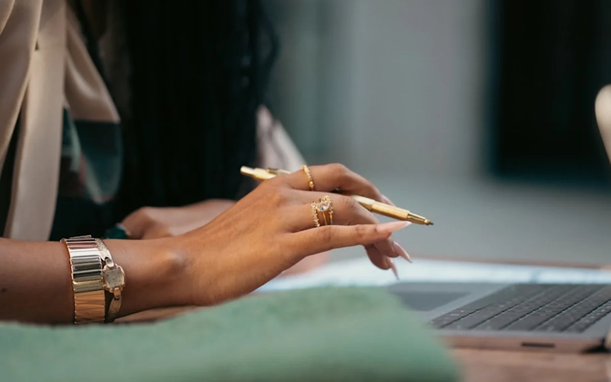 Hands with a gold pen resting on a laptop keyboard
