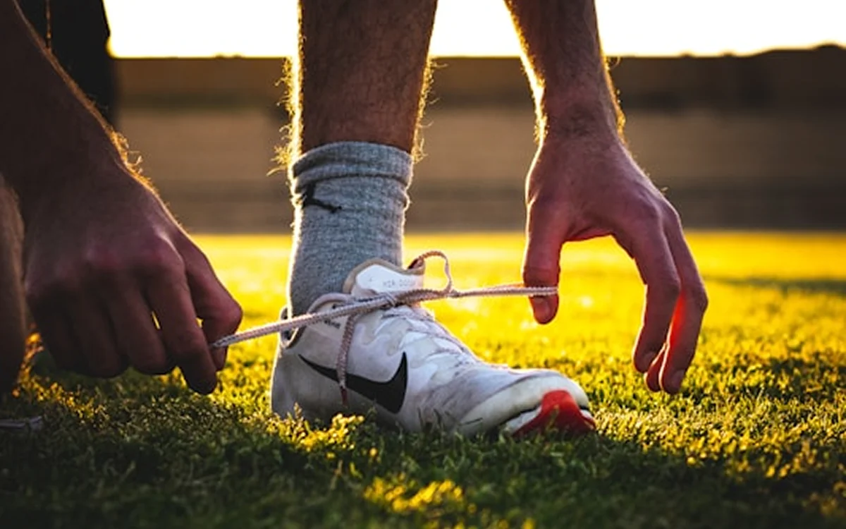 Footballer lacing a boot on floodlit grass