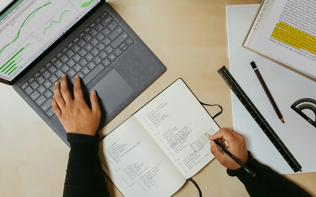 Overhead view of a laptop, open notebook and pencils on a desk