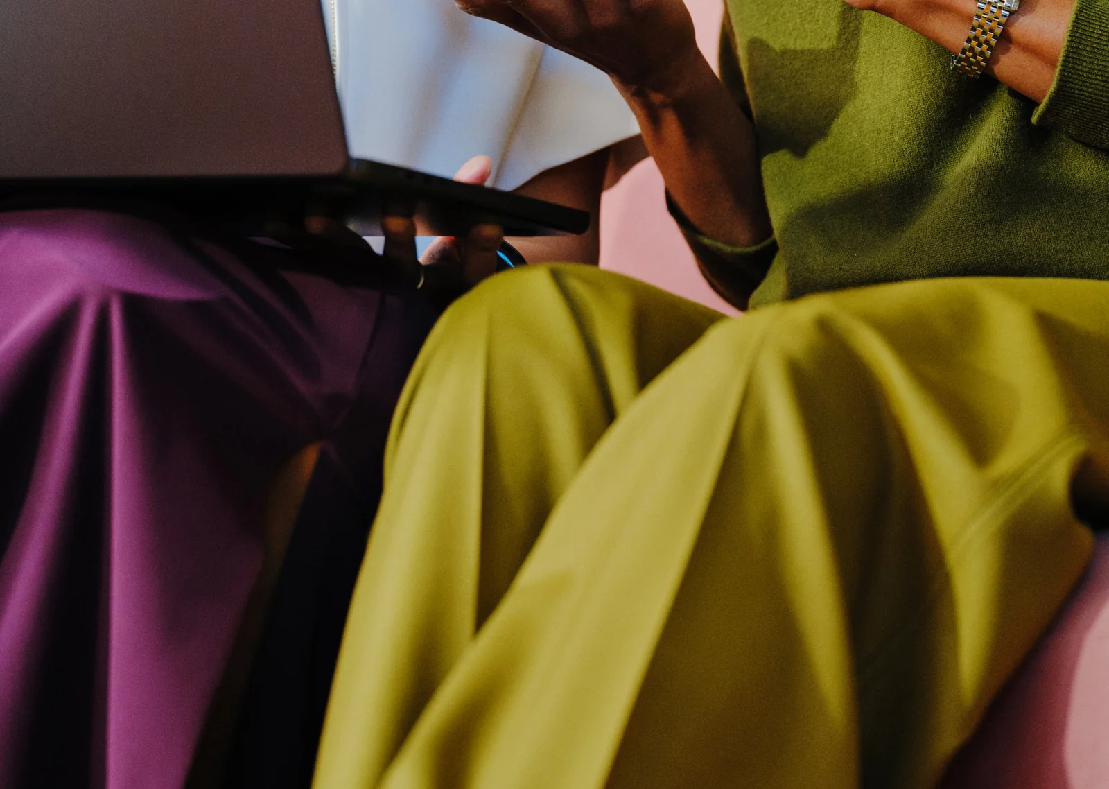 Two people working from a laptop, in purple and olive tailoring