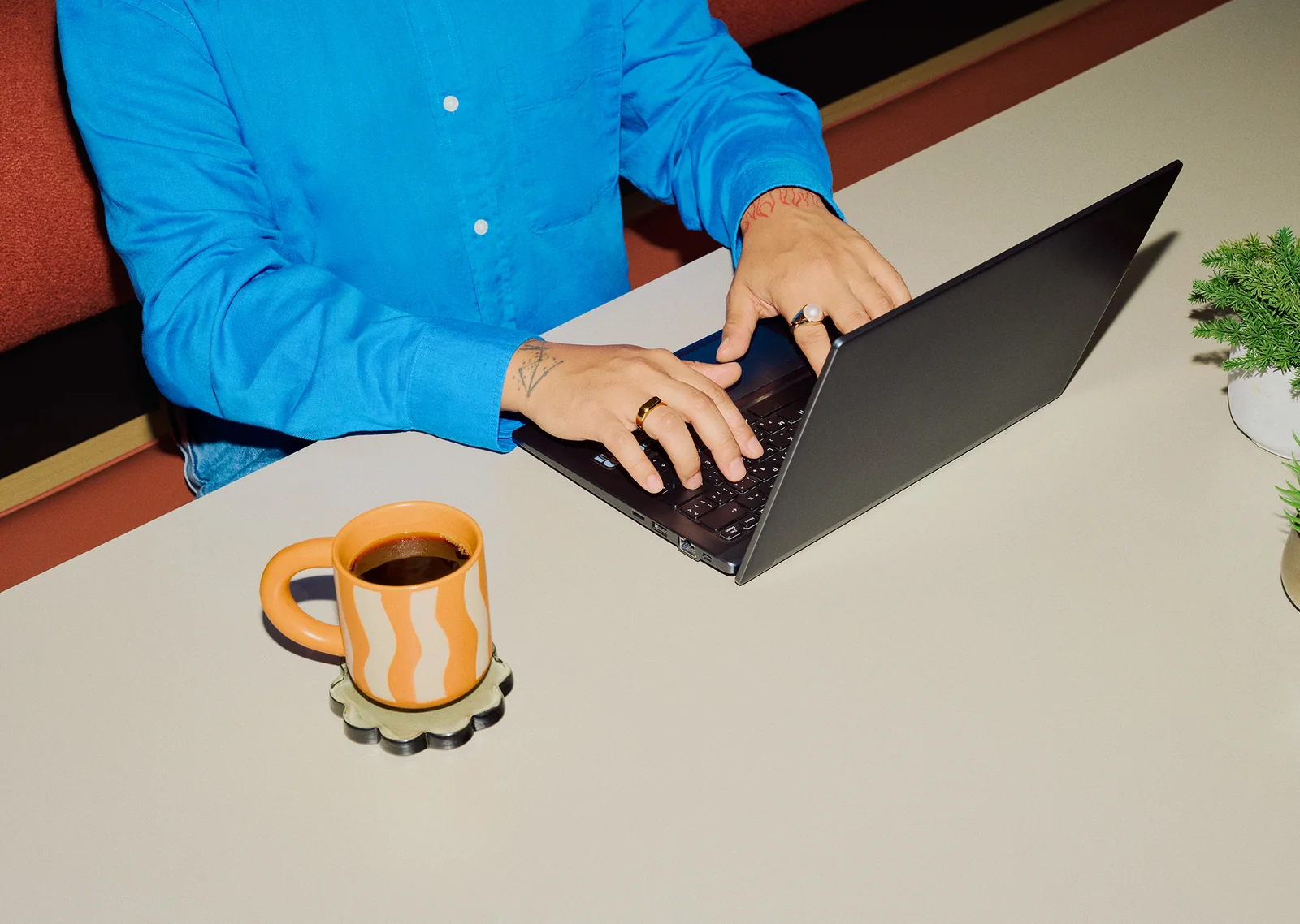 Person in a bright blue shirt typing at a laptop beside a striped mug