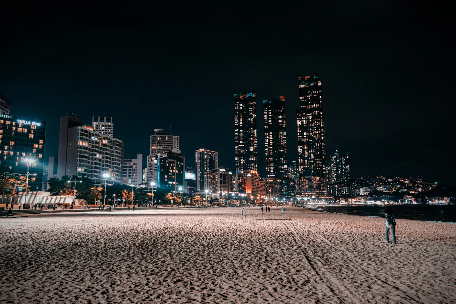 City skyline at night seen across an empty beach