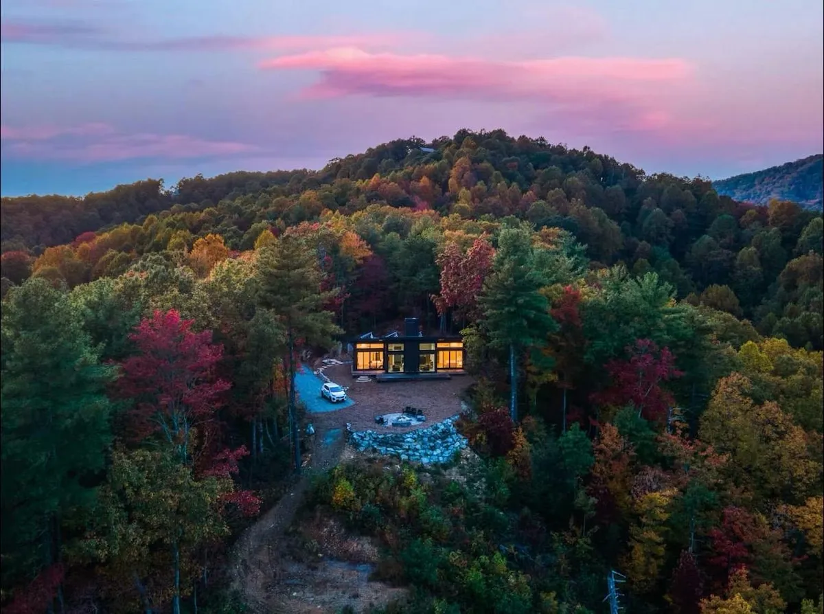 Aerial view of the Lost Ridge glass cabin alone on its ridge at dusk, surrounded by autumn forest