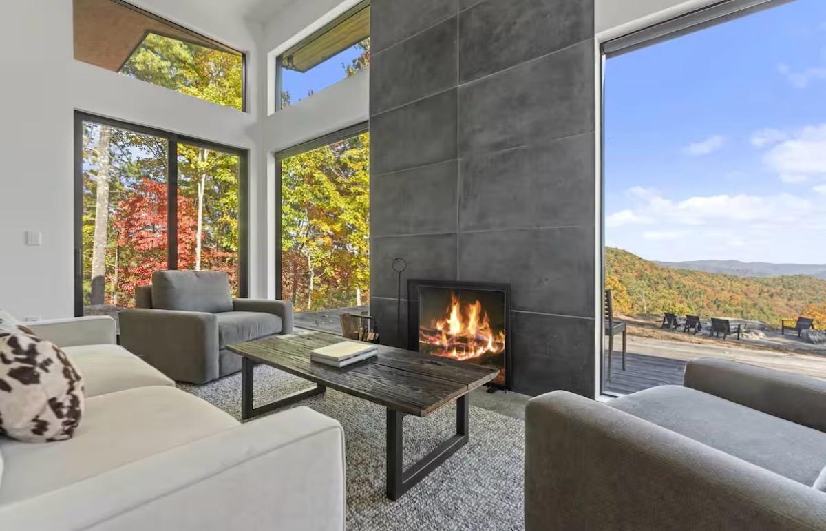 Wood fire burning in the two-story stone hearth, with red maples and mountains through the glass