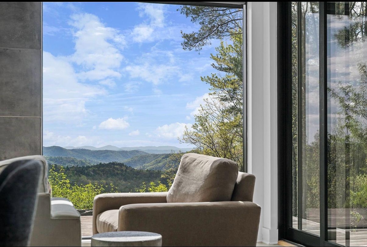 An armchair set against floor-to-ceiling glass looking out over layered blue ridges