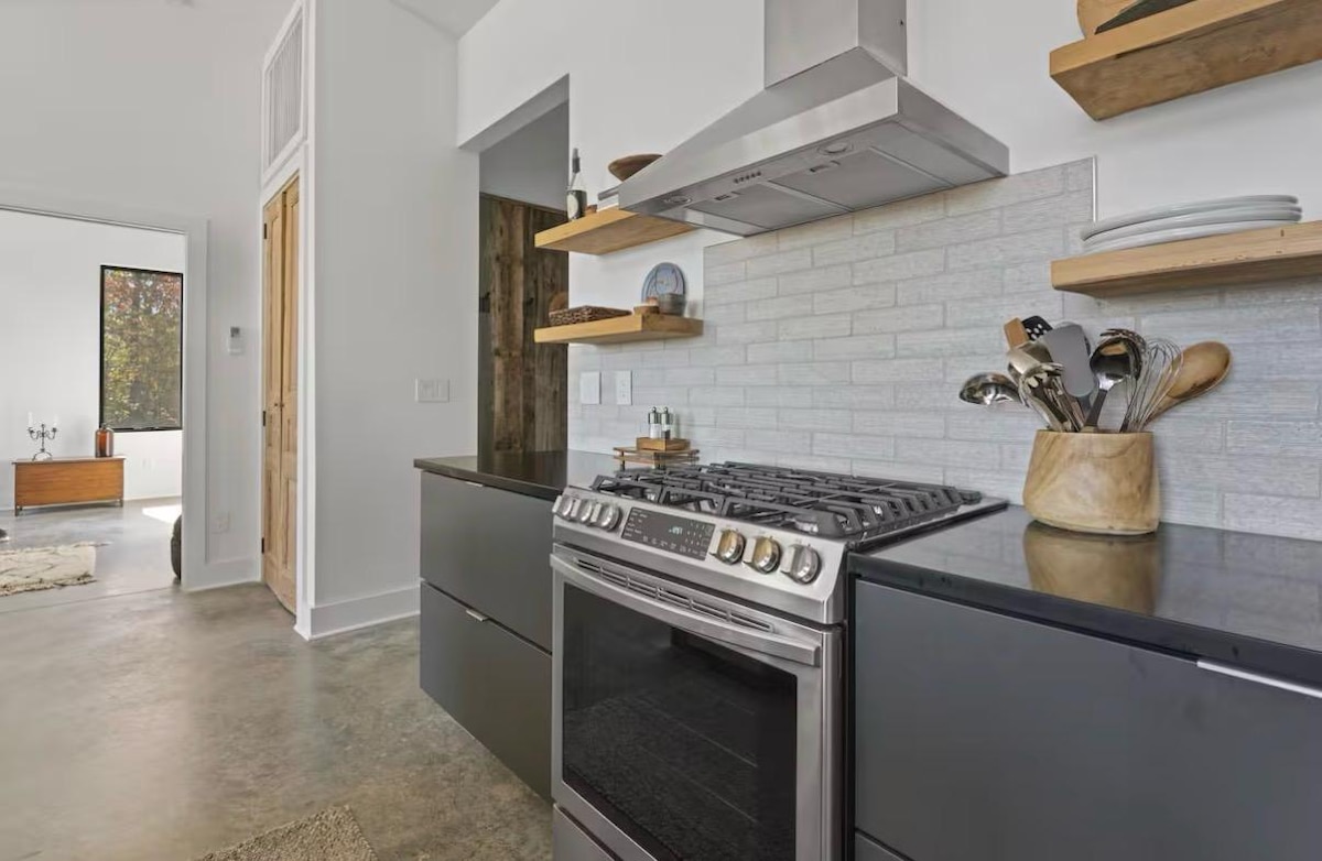 European stainless gas range beneath open shelving and white brick tile
