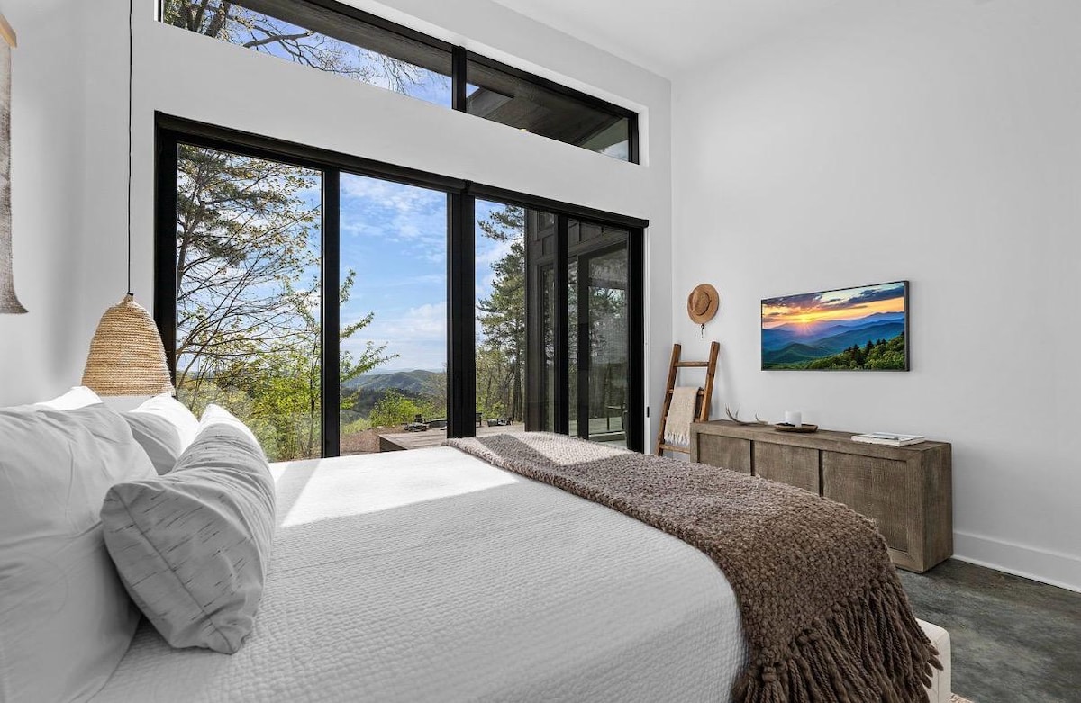 King bed with a linen throw, the Frame TV showing artwork, and spring green mountains outside