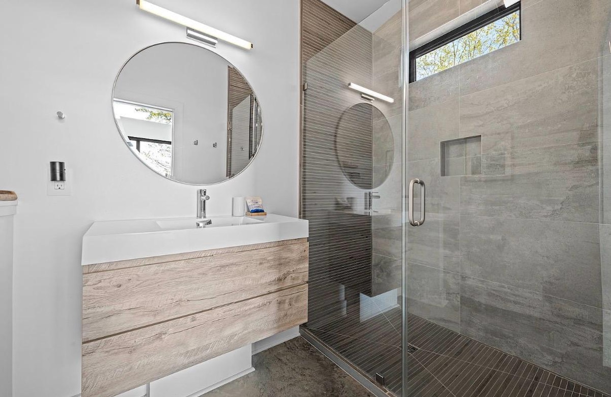 Bathroom with a round mirror, floating oak vanity, and a glass walk-in shower