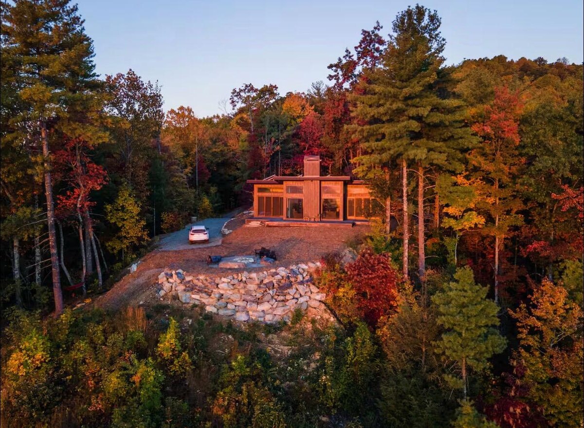 Lost Ridge lit from within at dusk, alone on its ridge above a stone wall and autumn forest