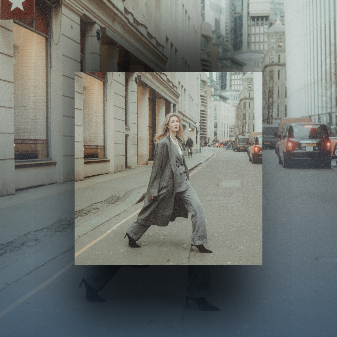 A woman in a grey coat crossing a city street, framed by a gold brand triangle.