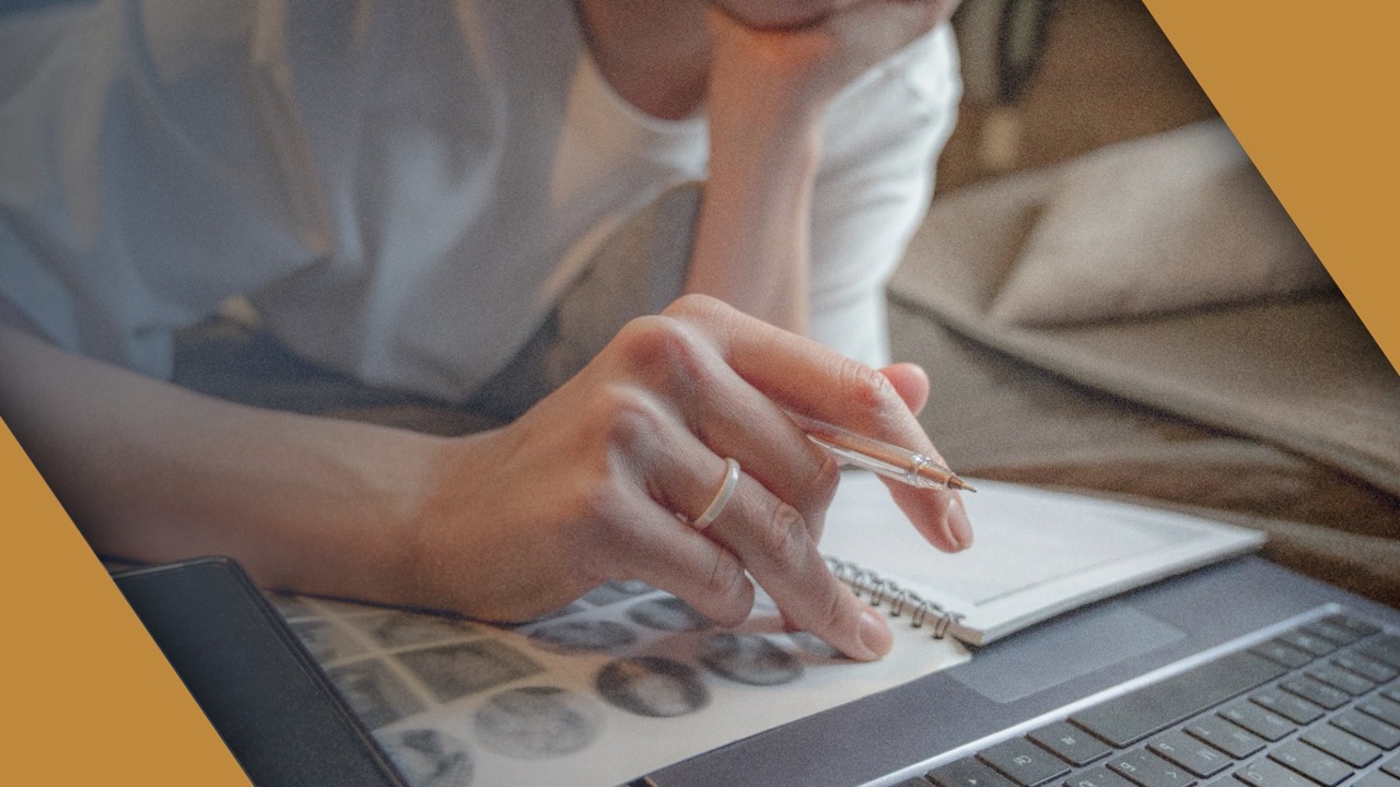 A person reviewing notes in a notebook on top of an open laptop.
