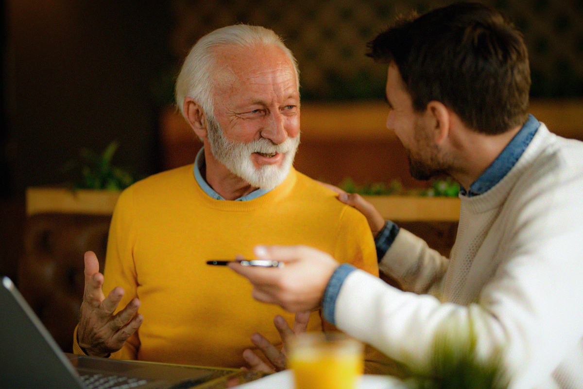 Adult son talking with his father at a table with a laptop
