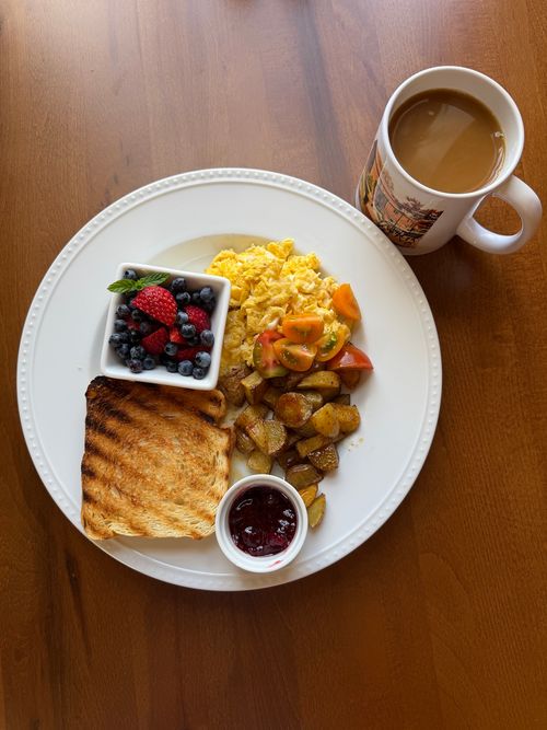 A photo of a plate with toast, eggs, and jam, alongside a mug of coffee