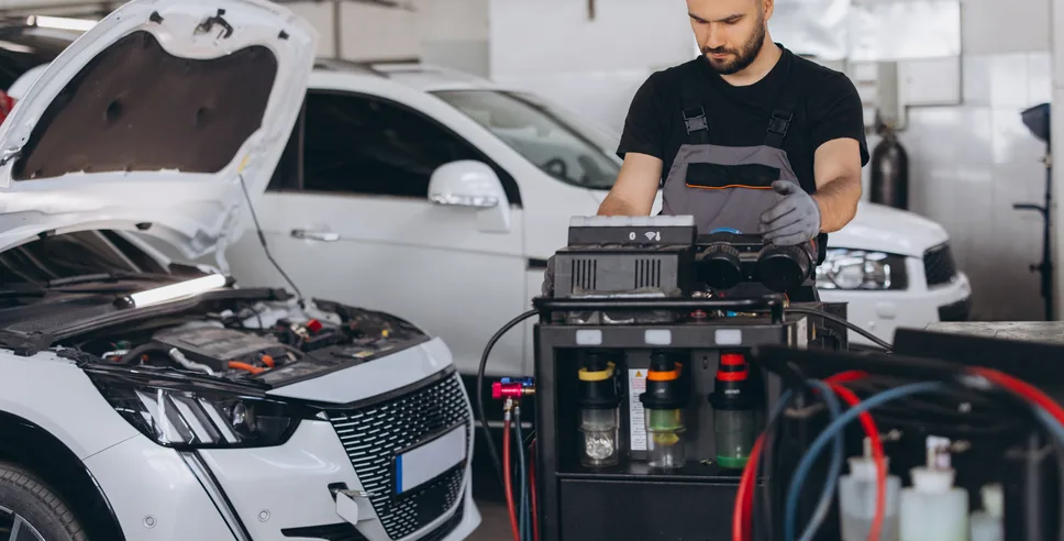 Technician working on a laptop in front of a white car with the hood open