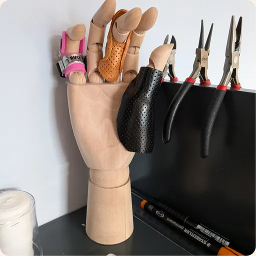 Holzmodell einer Hand mit Fingerschienen, daneben Werkzeug zur Schienenanpassung