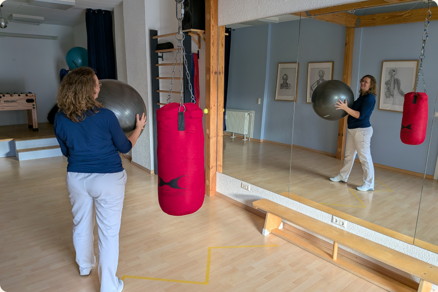 Übung mit einem Gymnastikball vor einem Spiegel im Bewegungsraum