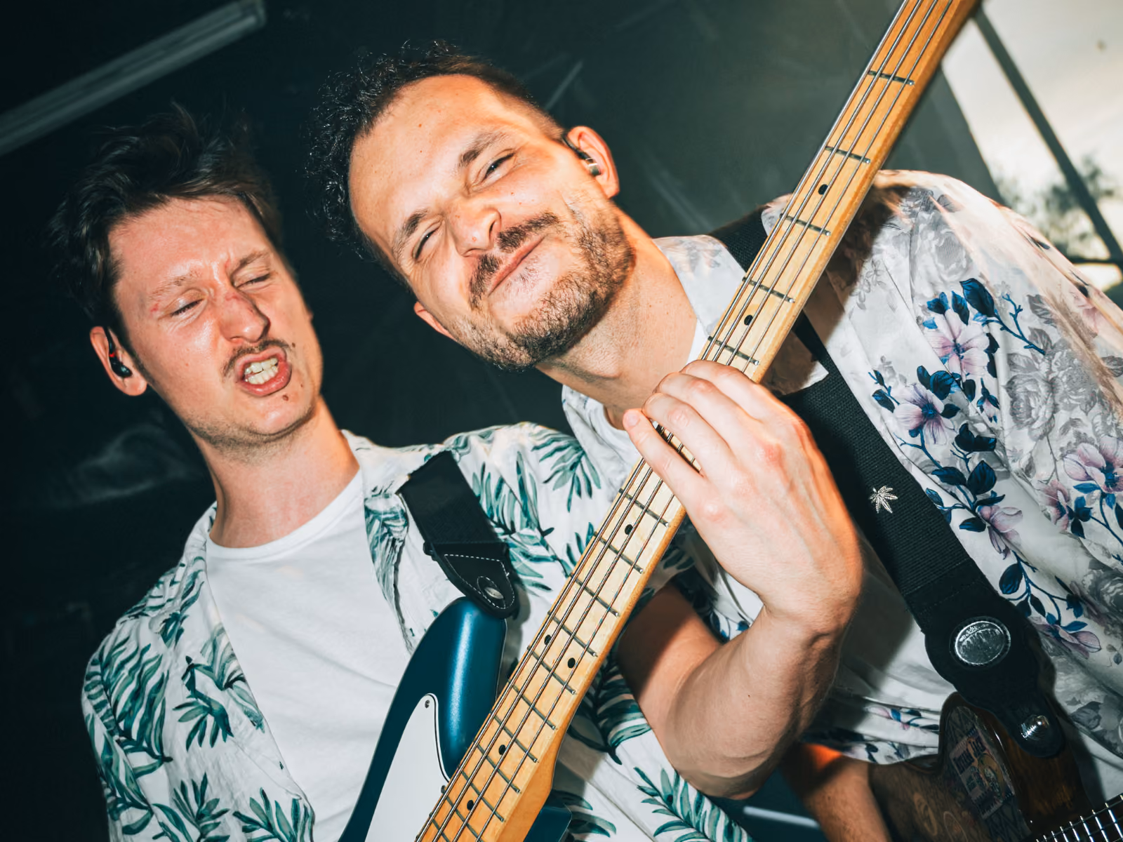 Twee mannen spelen gitaar samen op het podium, beiden met gezichten vol emotie en geconcentreerde blikken.