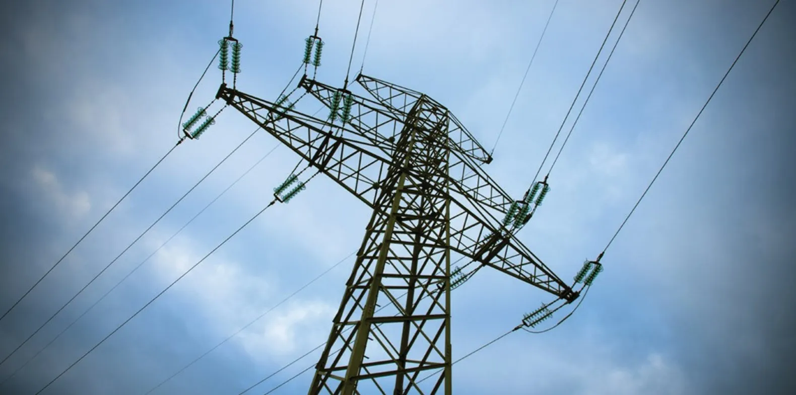 Close-up view of a high-voltage electricity transmission tower against a cloudy blue sky.