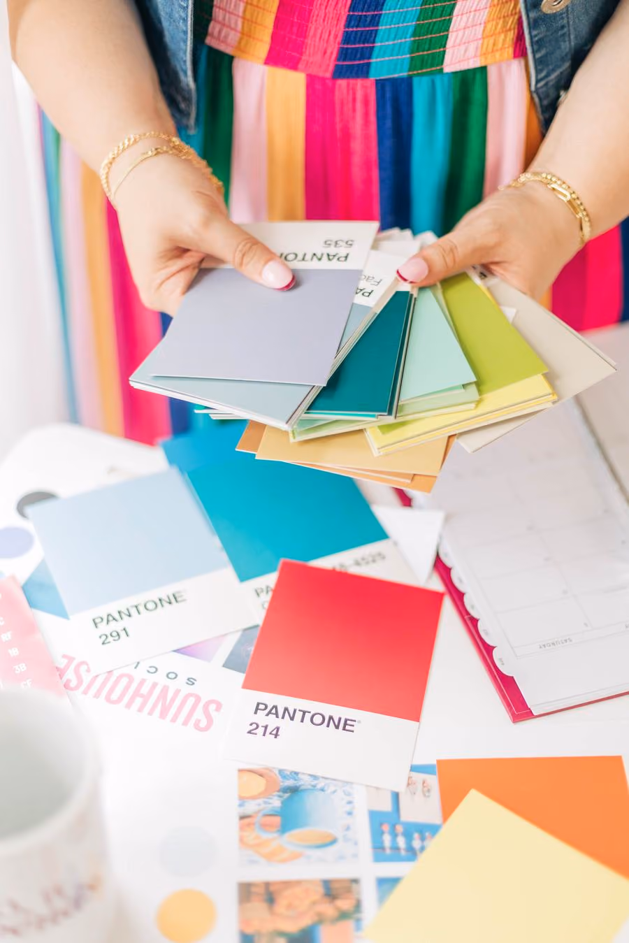 Kristine Gonzalez holding a fan of color swatches over a spread of printed layouts