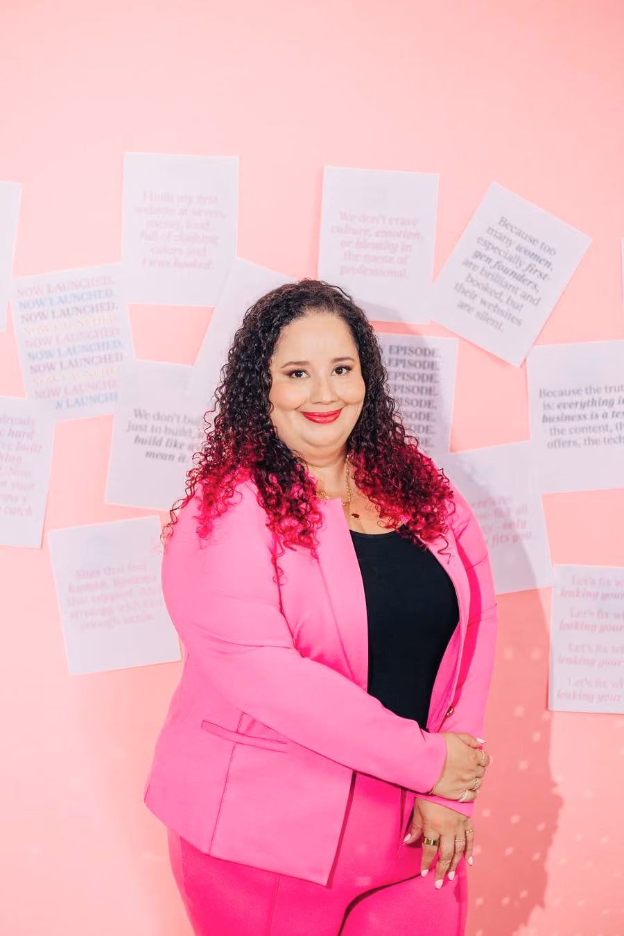 Kristine Gonzalez in a bright pink suit in front of a wall of printed notes