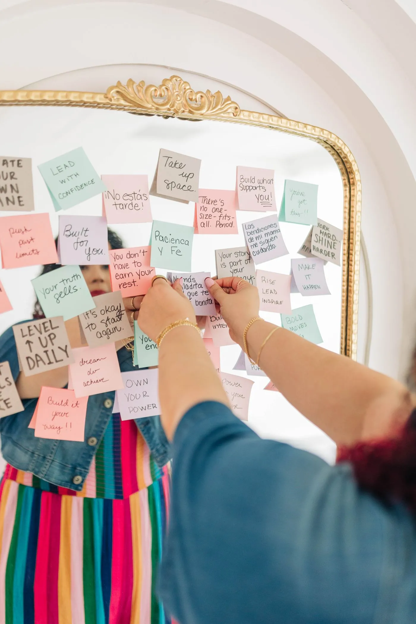 Kristine Gonzalez pinning handwritten sticky notes to a gold mirror