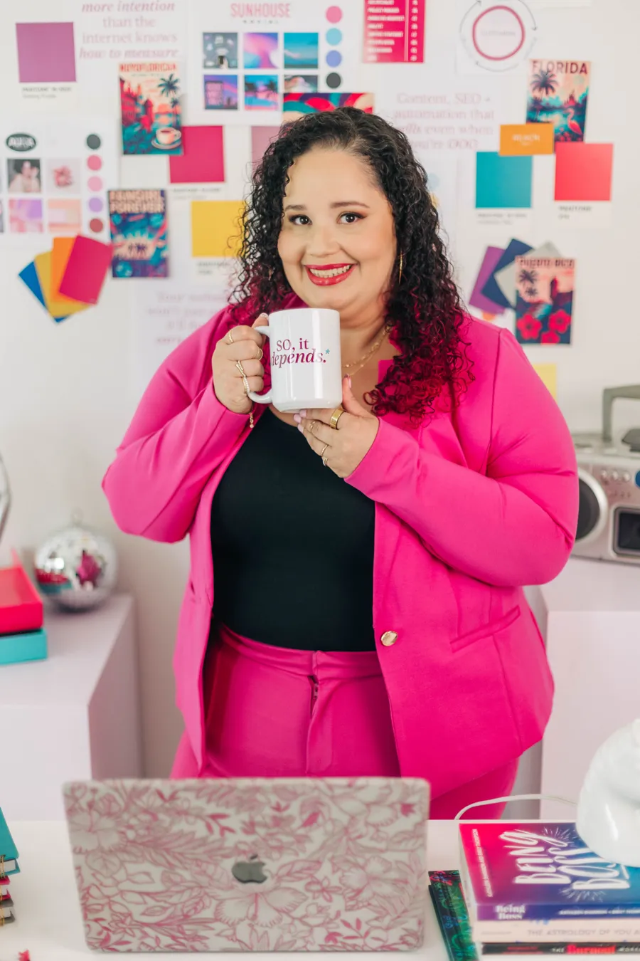 Kristine Gonzalez smiling at her desk, holding a So, It Depends mug with both hands