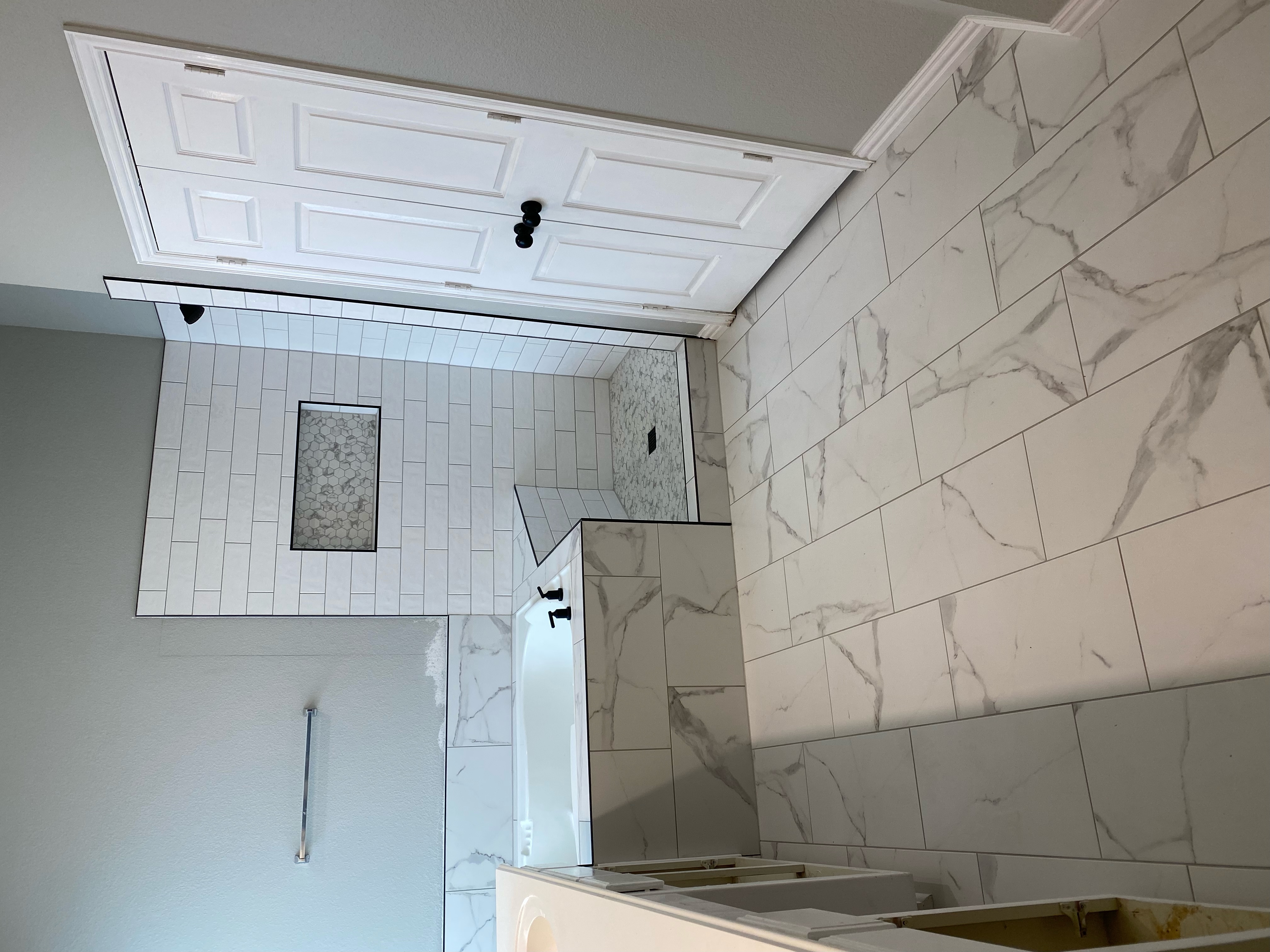 Completed North Richland Hills shower remodel with white subway tile and marble-look porcelain by Redcrest Construction