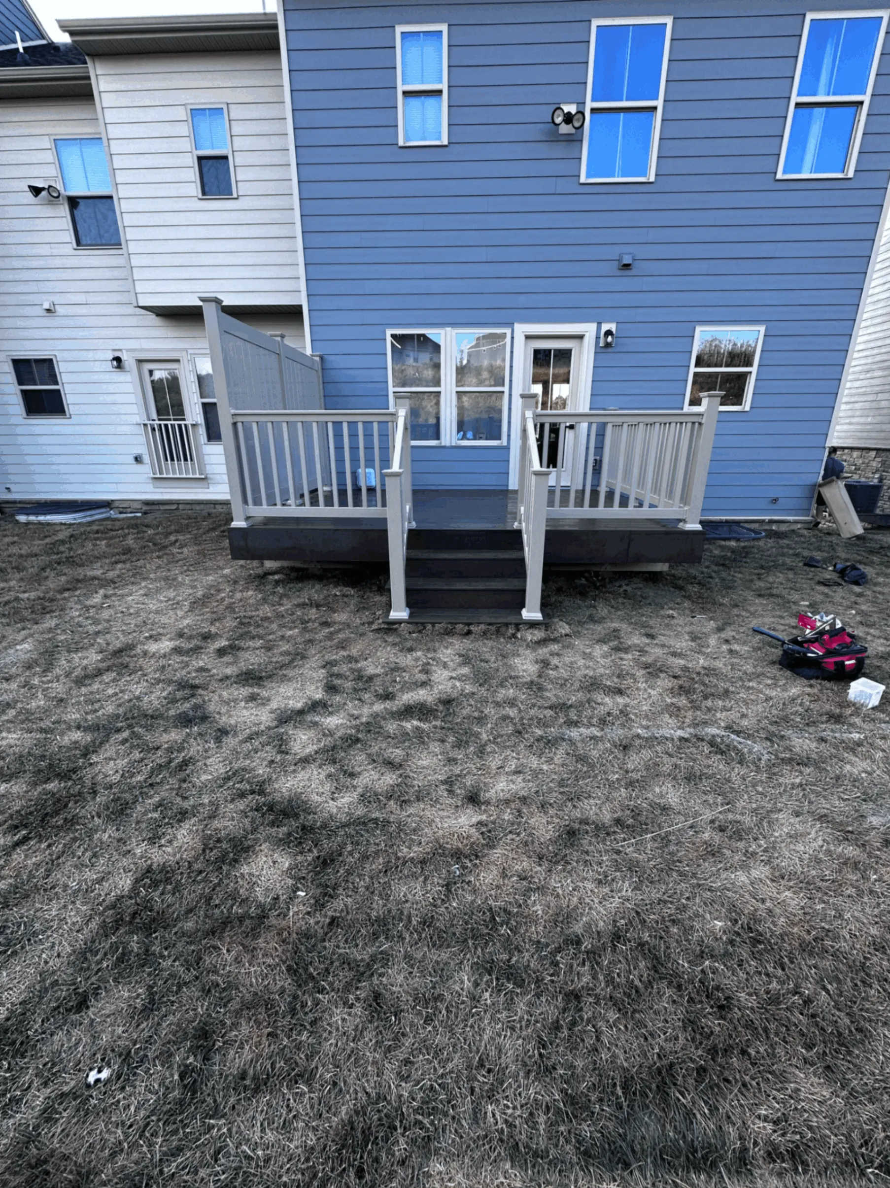 Rear deck with gray railings and entry steps on a two-story blue home