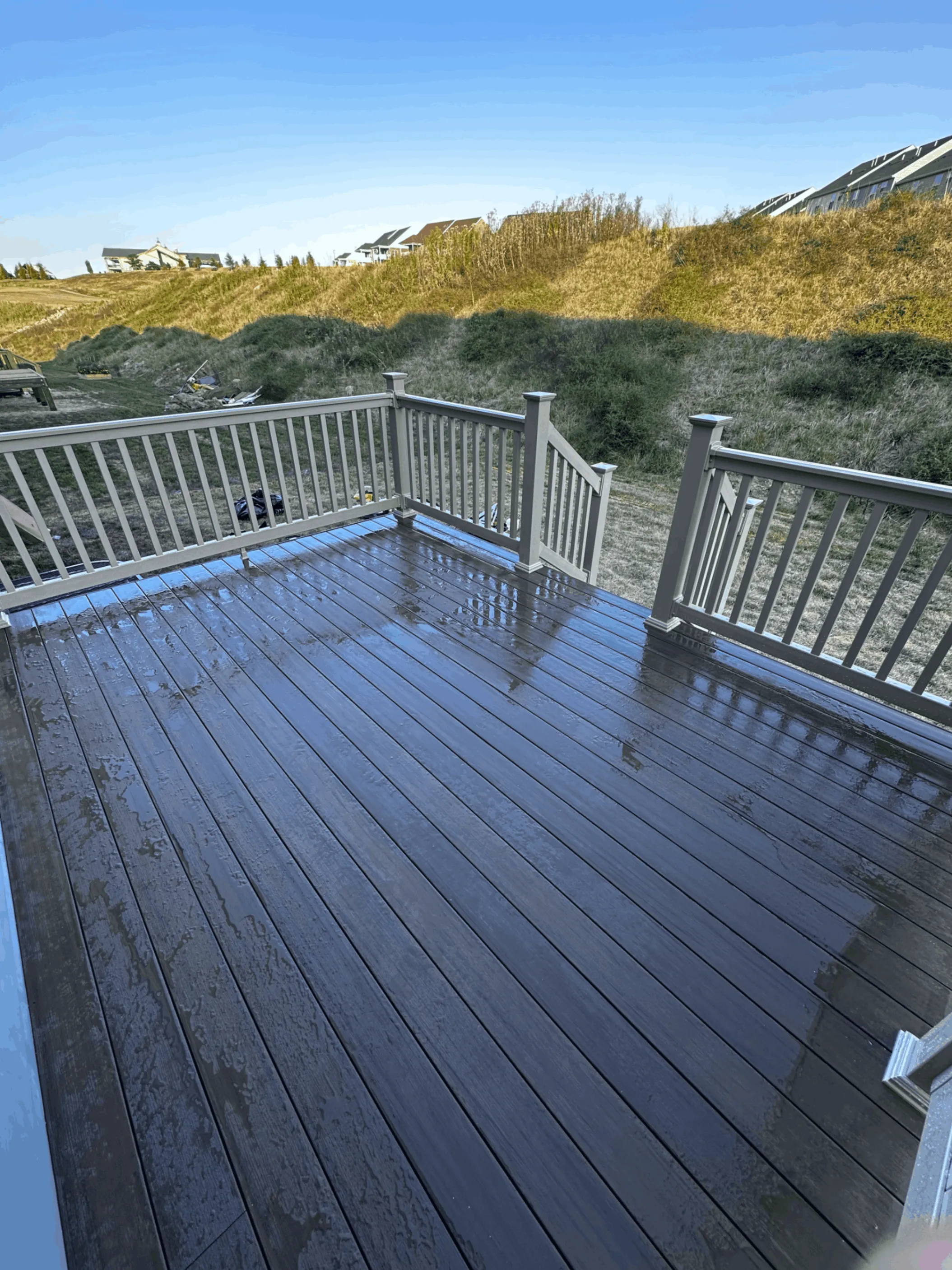 Wet gray composite decking with gray railings above a sloped hillside