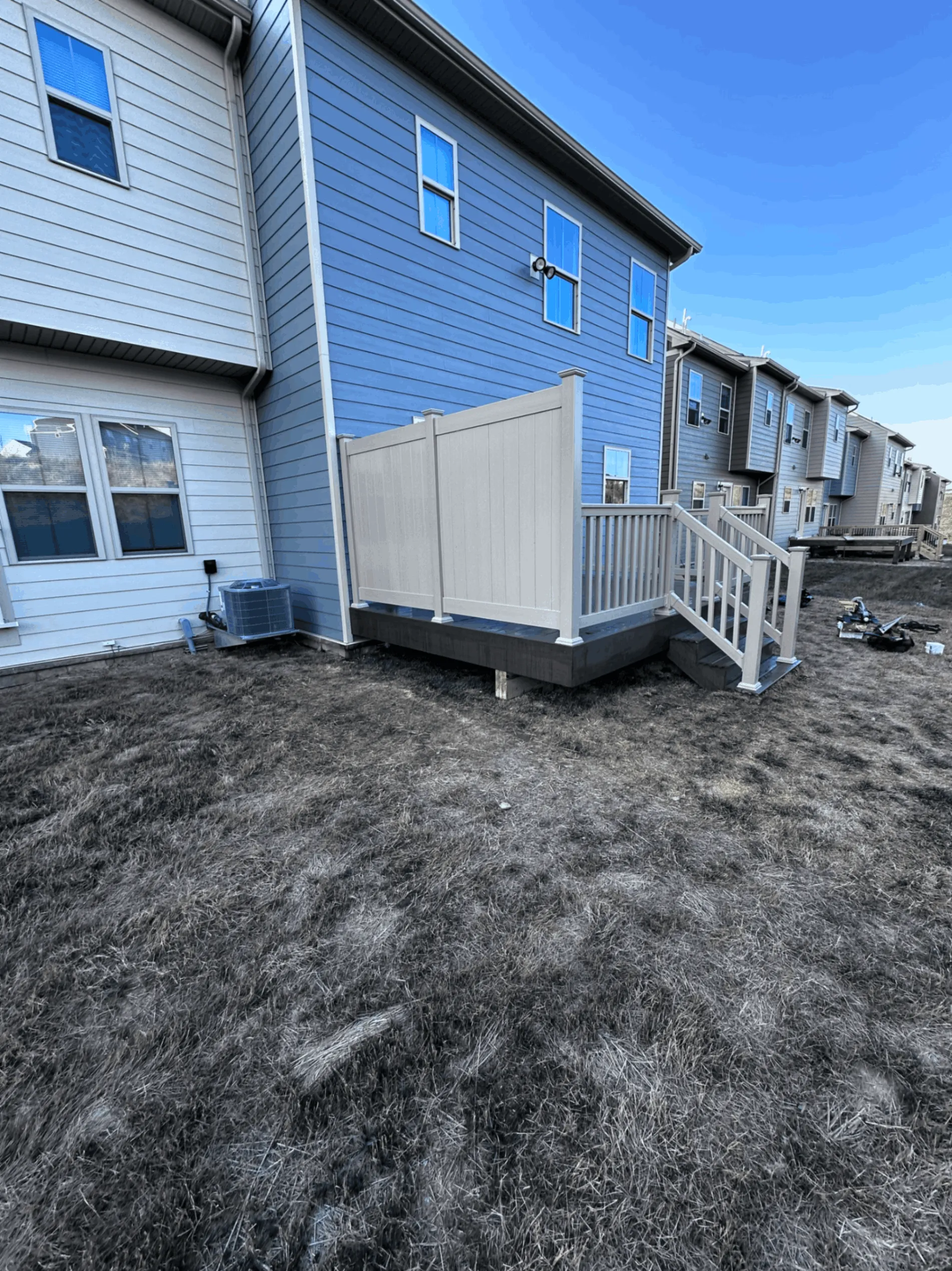 Gray deck with a privacy panel and railings at the rear of a blue townhome