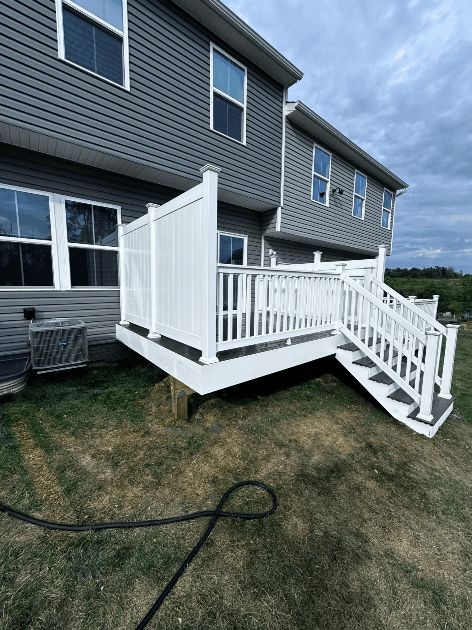 Rear deck with white vinyl railings and stairs on a gray sided home